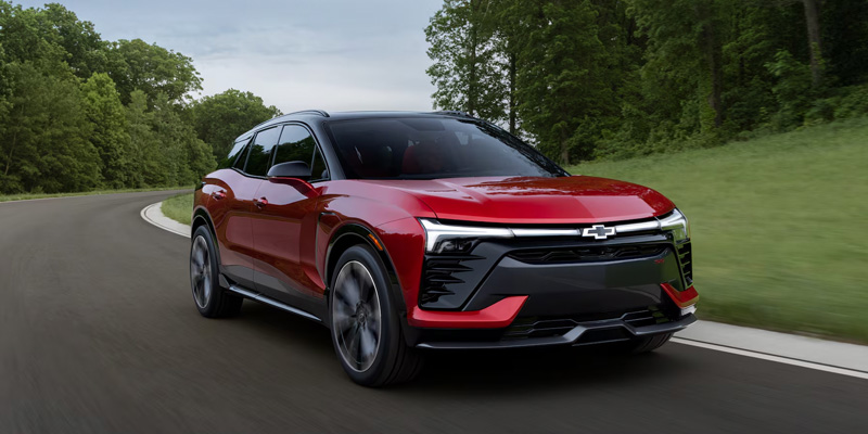 Red 2026 Chevrolet Blazer EV driving along a scenic road, showcasing its sleek electric design, modern styling, and dynamic performance in Bridgewater, NJ.
